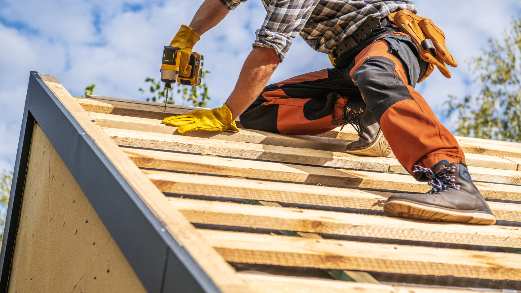 Construction worker installing wooden roof panels with power drill